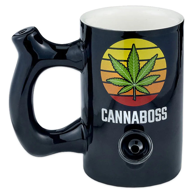 A black ceramic smoking pipe shaped as a mug with a weed leaf decal on top of a sunset background and the word cannaboss underneath.