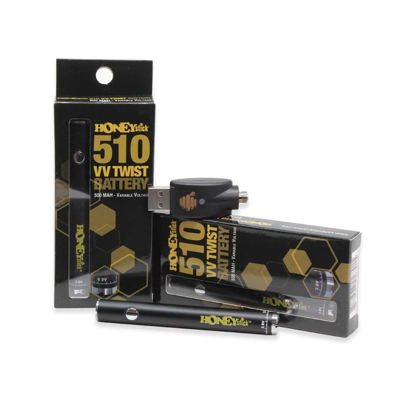 Honeystick's 510 thread matte black vape cartridge battery. Laying next to two display boxes that showcase the retail packaging and the usb charger sits on top.