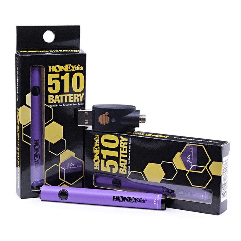 Honeystick's 510 thread purple vape cartridge battery. Laying next to two display boxes that showcase the retail packaging and the usb charger sits on top.