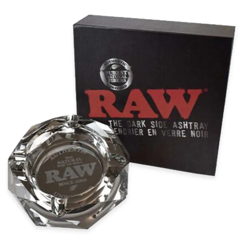 RAW's Dark Side Glass Ashtray. A dark gray glass ashtray in a crystal like construction. Authentic RAW branding in the middle. RAW's Dark Side Glass Ashtray display box. a Black RAW box with silver accents.