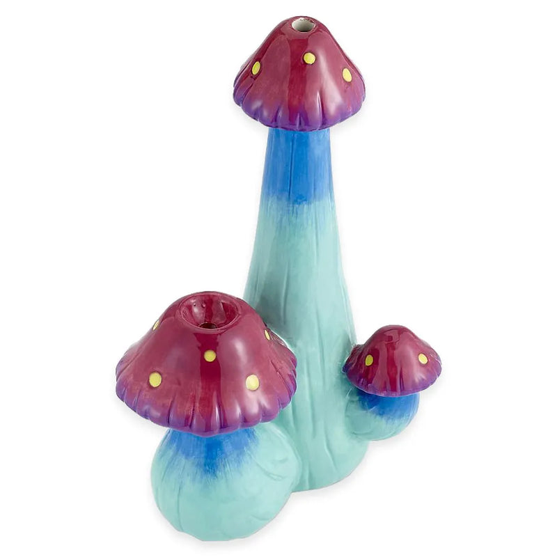 A smoking pipe shaped as 3 mushrooms and made from ceramic. Deep hues of blue and shades of green with a pinkish purple mushroom head that has yellow spots.