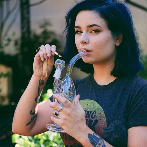How to Level Up Your Cheap Dab Rig blog cover photo. Photo showcases a young dark haired girl looking at the camera while taking a puff from her dab right in hand.