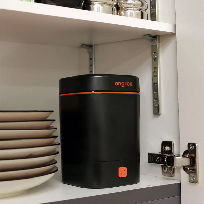 Ongrok's decarboxylator machine sitting next to a stack of 8 dinner plates in an open kitchen cupboard.