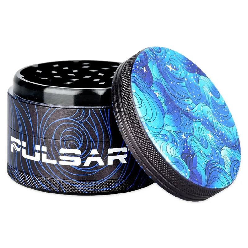 Pulsar's Design Series Metal Grinders feature the Space Dust design, depicting an ever-flowing blue depth lit by distant sparkling stars, with matching side art. Open grinder showcasing the metal lid and sharp diamond shaped cutting teeth second chamber.