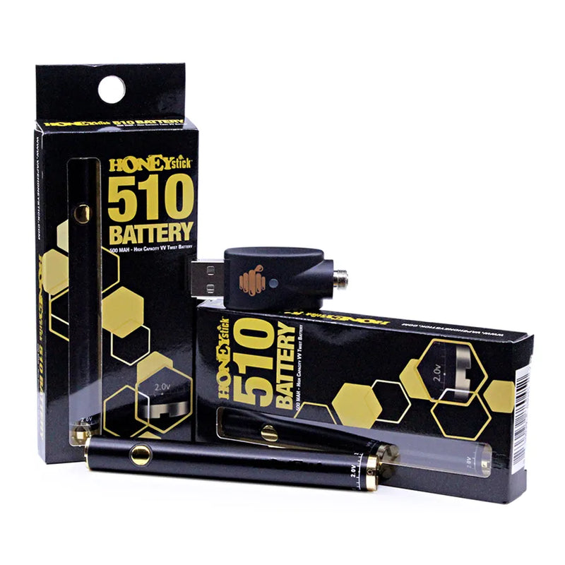Honeystick's 510 thread black vape cartridge battery. Laying next to two display boxes that showcase the retail packaging and the usb charger sits on top.