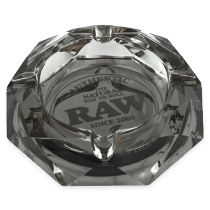 RAW's Dark Side Glass Ashtray. A dark gray glass ashtray in a crystal like construction. Authentic RAW branding in the middle. Image showcases how it would look flat on a table.