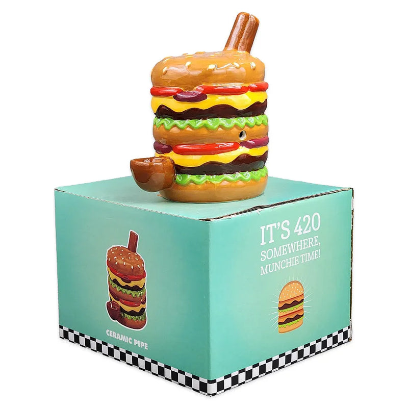 A smoking pipe made from ceramic in the shape of a double stacked hamburger on top of its display box.